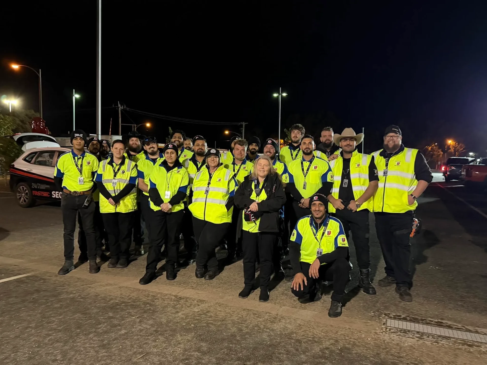 Large Fastsec Security team in hi-vis vests gathered beside a patrol vehicle at night