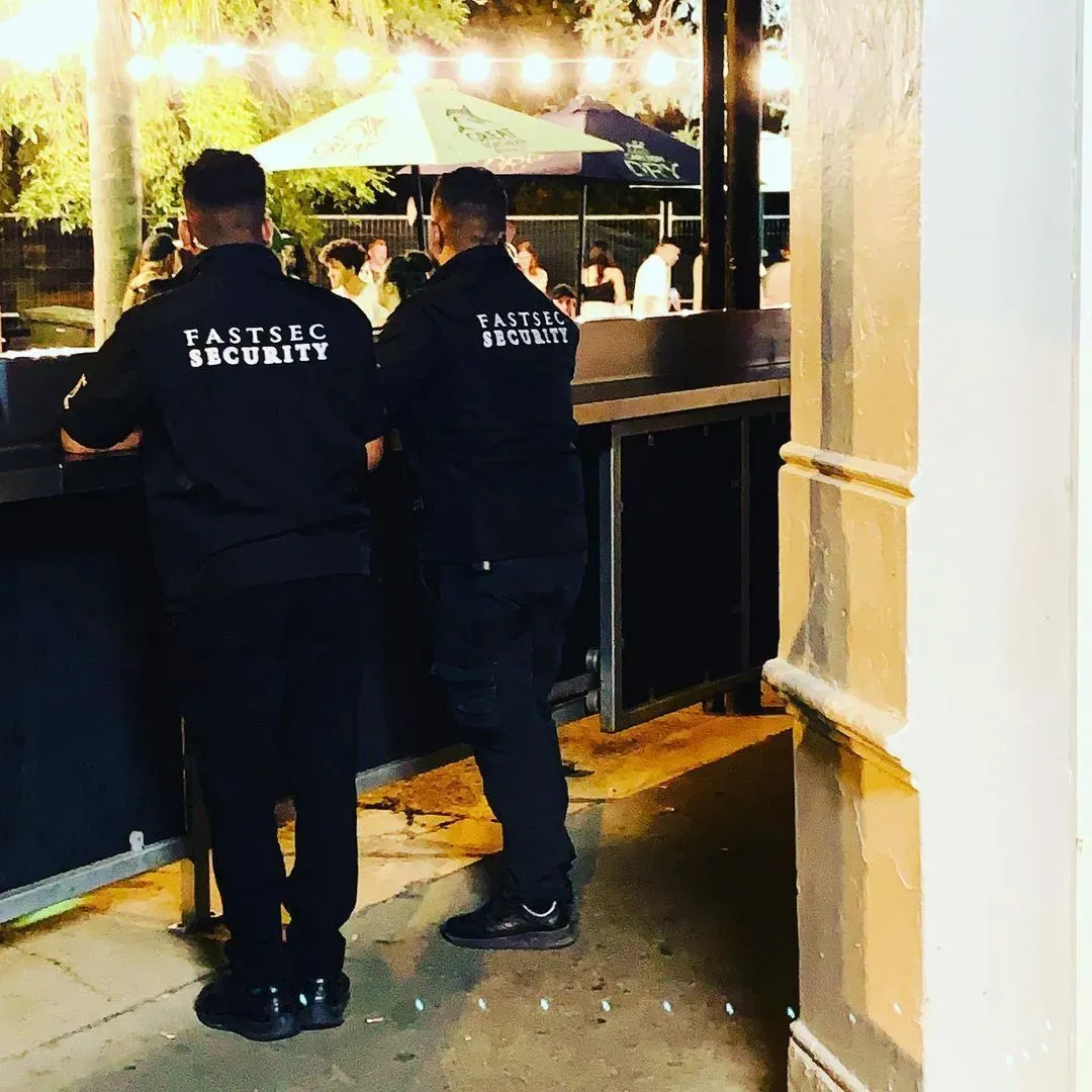 Two Fastsec Security guards in branded jackets watching a venue courtyard at night